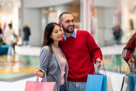 Cheerful international couple shopping for new clothes at city mall, looking at store windowの写真素材