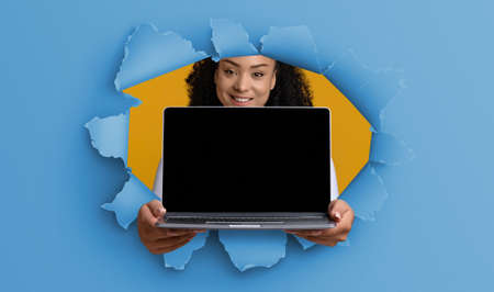 Black young lady showing empty laptop screen through torn paper