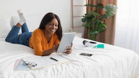 Black Female Using Tablet Computer Lying On Bed In Bedroom