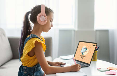 Remote Education. Teen Schoolgirl Wearing Wireless Headphones Study With Laptop At Home