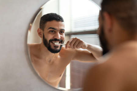 Handsome young Arab man using toothbrush in bathroomの写真素材