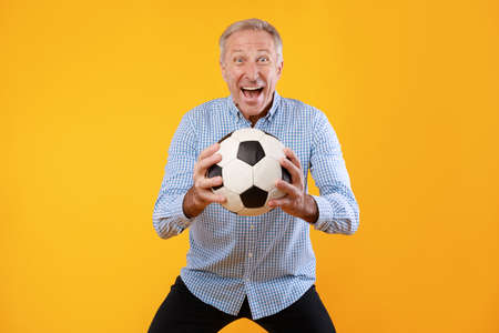 Mature man posing with soccer ball on yellow backgroundの写真素材