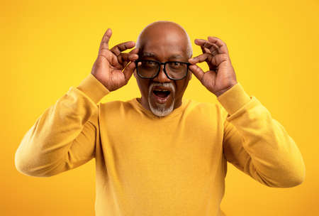 Portrait of senior African American man in glasses opening mouth in excitement, cannot believe huge...