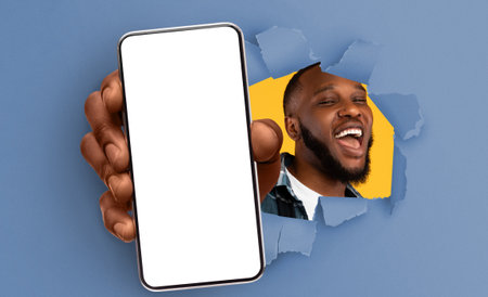 Black guy showing white empty smartphone screen through torn paperの写真素材