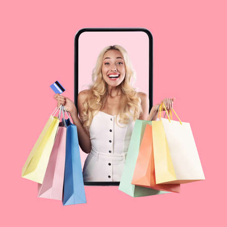 Lady looking out phone holding credit card and shopping bagsの写真素材