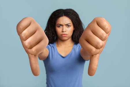 Serious black lady showing thumbs-down on blue studio backgroundの写真素材
