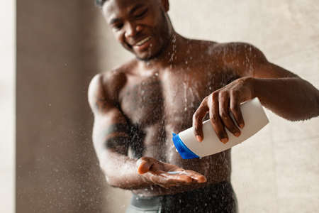 Handsome Black Guy Taking Shower Squeezing Shampoo Bottle In Bathroomの写真素材