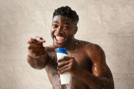 Black Man Singing With Shampoo Bottle Taking Shower In Bathroomの写真素材