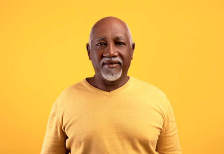 Portrait of happy elderly black man looking at camera over orange studio backgroundの写真素材