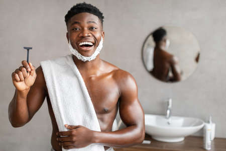 Excited Black Man Holding Safety Razor In Bathroomの写真素材