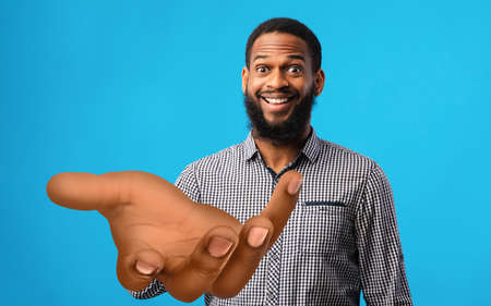 Surprised young black man standing with big outstretched hand on blue studio background, mockup for your productの写真素材