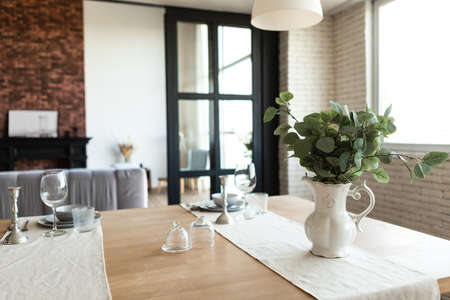 Vase with plant leaves and dishware on table in dining room or kitchen interior. Scandinavian style...