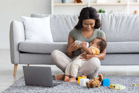 Maternity Leave Concept. Young Black Mother Giving Bottle With Water To Babyの写真素材