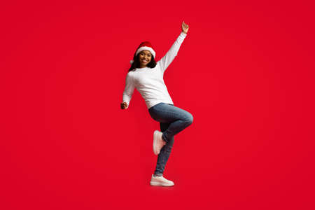Attractive african american woman in Santa hat dancing on redの写真素材