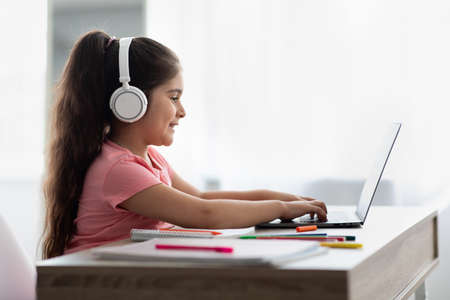 Online Education. Little Middle Eastern Girl In Headphones Using Laptop At Home