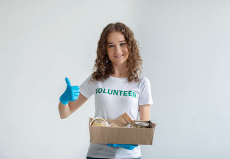 Excited activist volunteer holding box with donations and showing thumb up, smiling at camera over light backgroundの写真素材