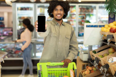 Black Guy Showing Smartphone Blank Screen Shopping Groceries In Supermarketの写真素材