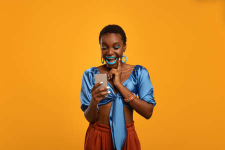 Emotional black woman in bright outfit using smartphoneの写真素材