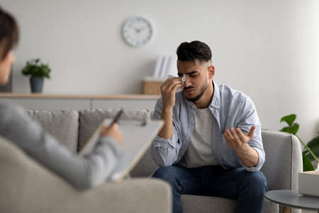 Depressed middle eastern guy crying at psychotherapists office, seeking professional help, sharing his problemsの写真素材