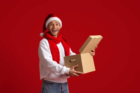Christmas Delivery. Surprised Young Guy In Santa Hat Opening Parcel Box