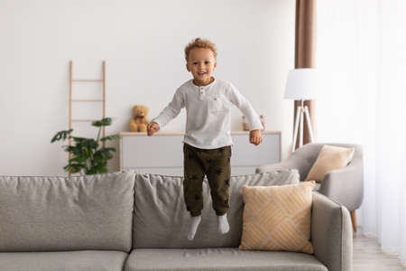 Cheerful African American Little Boy Jumping Having Fun At Homeの写真素材