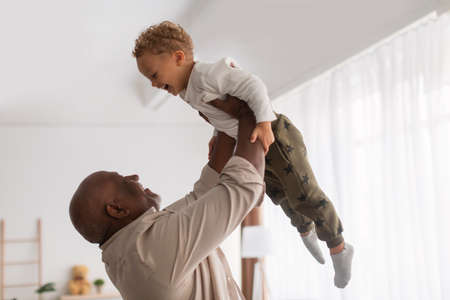 African Grandpa Holding Little Grandson Up In Air At Homeの写真素材