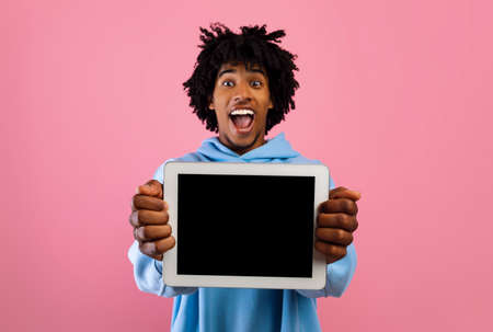 Overjoyed black teenager showing digital tablet with mockup for website or app design on pink backgroundの写真素材