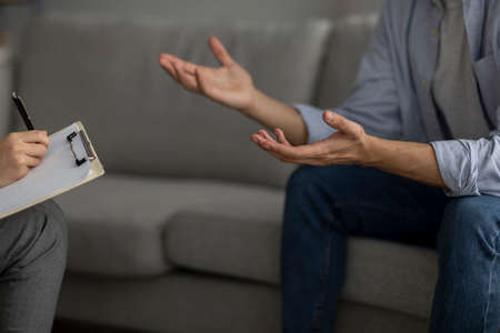 Unrecognizable man talking to psychotherapist, sitting on sofa and having consultation with counsellor, closeupの写真素材