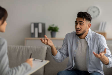 Stressed and emotional arab man suffering from depression, counselor providing professional assistance at medical officeの写真素材