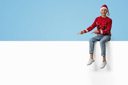 Funny Guy In Santa Hat Sitting On Top Of Blank Advertisement Boardの写真素材