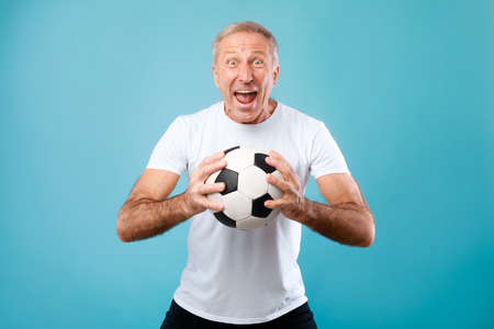 Mature man posing with soccer ball on blue backgroundの写真素材