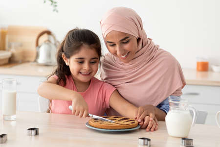 Cute Little Girl And Her Muslim Mother Cutting Homemade Pie In Kitchenの写真素材