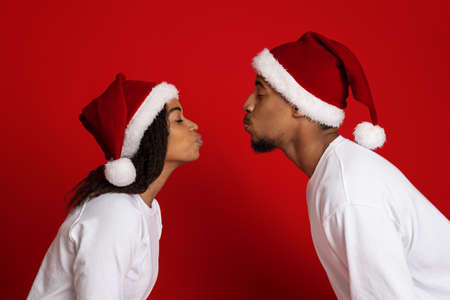 Black man and woman in Santa hats kissing on redの写真素材