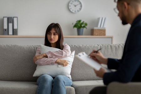 Psychotherapist consulting unhappy middle eastern lady, having therapy session at clinic, woman hugging pillowの写真素材