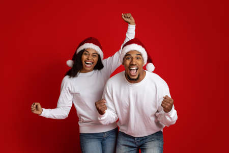 Emotional black couple in Santa hats gesturing on redの写真素材