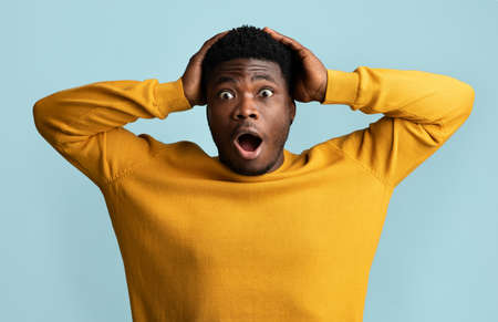 Puzzled african american guy looking at camera, gesturing on blueの写真素材