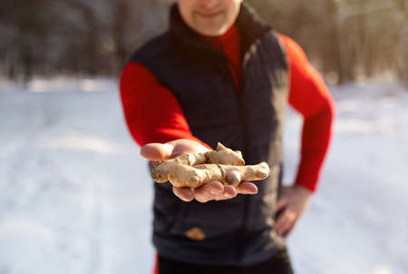 Natural health care concept. Cropped view of senior man in sportswear holding ginger root in winter parkの写真素材