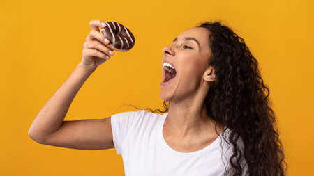 Happy Latin Lady Holding Doughnut Biting Cake At Studio