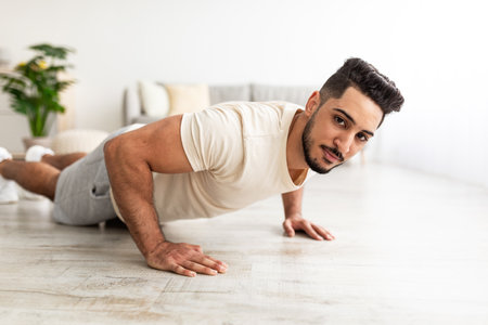 Attractive young Arab man standing in plank pose or doing push ups on mat at homeの写真素材