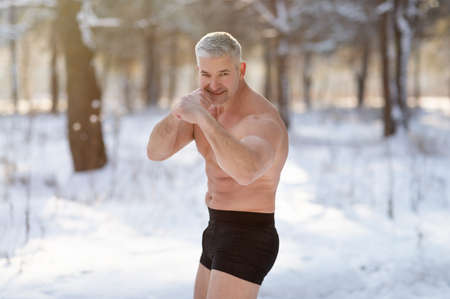 Handsome senior man with bare chest standing in fighter pose in winter forest. Acclimation conceptの写真素材