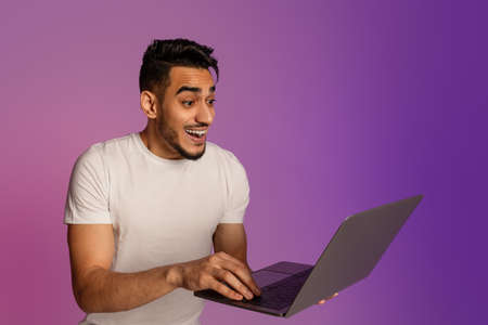 Excited young Arab guy looking at laptop screen, shocked over big online lottery win or success in...