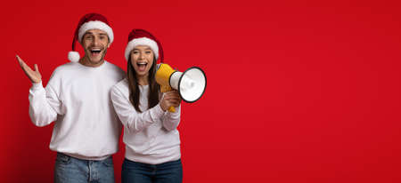 Xmas Ad. Joyful Couple In Santa Hats Making Announcement With Megaphone