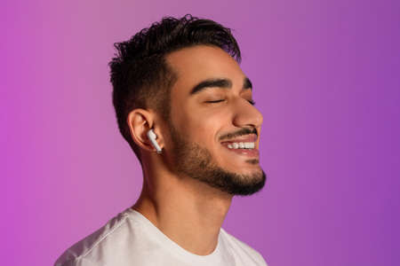 Handsome young Arab guy in casual outfit listening to music in earphones, closing eyes and relaxing...