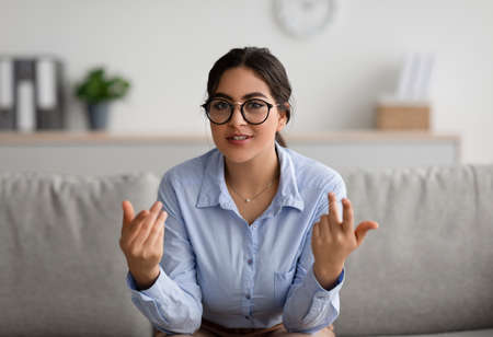 Cheerful young middle eastern female psychologist talking to camera and gesturing during therapy session at clinicの写真素材