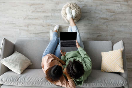 Top view of millennial Asian couple sitting on couch with laptop at home, mockup for website design on pc screenの写真素材