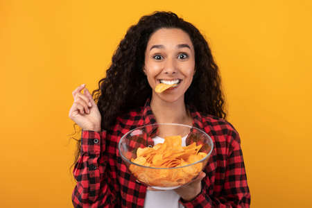 Excited Latin Lady Eating Delicious Potato Crispsの写真素材