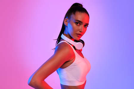 Attractive Sporty Woman With Wireless Earphones Posing On Neon Backgroundの写真素材