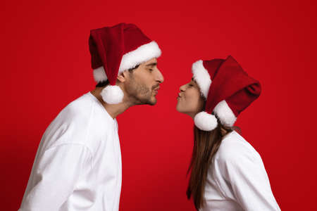 Xmas Kiss. Man And Woman In Santa Hats Kissing Over Red Backgroundの写真素材