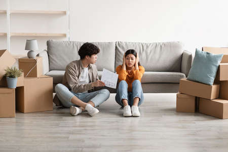 Unhappy Asian couple having argument over house rental or purchase documents in their new apartment on moving dayの写真素材