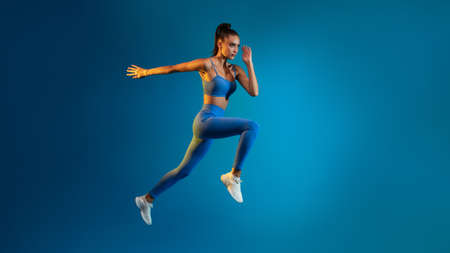 Fitness Woman Jumping In Mid-Air Over Blue Background, Panorama, Full-Lengthの写真素材
